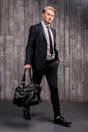 Stylish handsome. Full length of handsome young man in formalwear carrying a black bagの写真素材