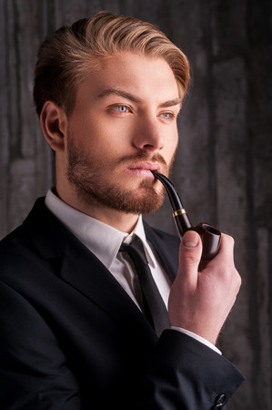 Smoking a pipe. Portrait of handsome young man in formalwear smoking a pipe and looking awayの写真素材