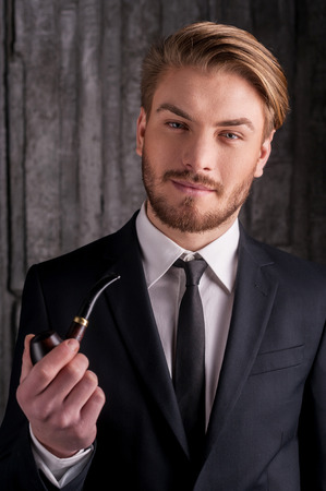 Man with a smoking pipe. Portrait of handsome young man in formalwear holding a smoking pipe and smiling at camera の写真素材