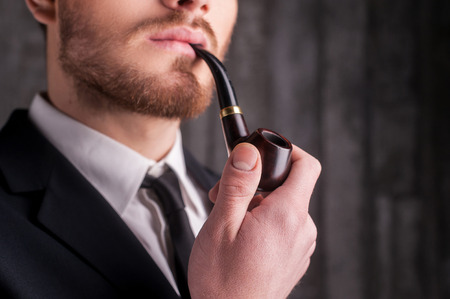 Smoking a pipe. Cropped image of handsome young beard man in formalwear smoking a pipe and looking awayの写真素材