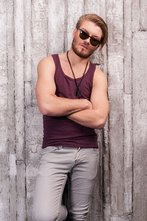 Looking trendy. Handsome young man in sunglasses leaning at the wall and looking at cameraの写真素材