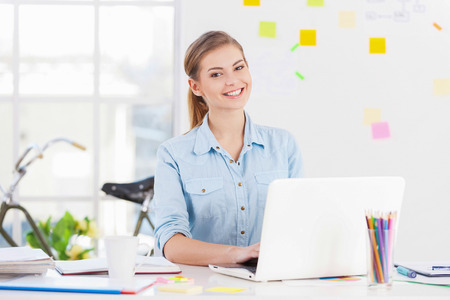 Businesswoman at work. Cheerful young businesswoman in casual wear using computer and smiling while sitting at her working placeの写真素材