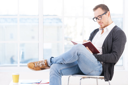 Handsome bookworm. Thoughtful young man in shirt sitting on the chair and reading a book の写真素材