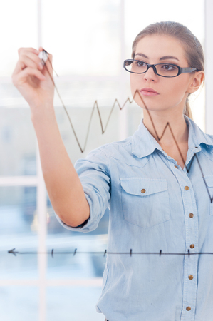 Attractive businesswoman drawing a graph  An attractive businesswoman analyst drawing a graph on a clear class wallの写真素材