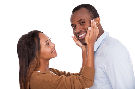 I know she loves me. Handsome young African man looking at camera and smiling while his girlfriend standing close to him and touching his face の写真素材