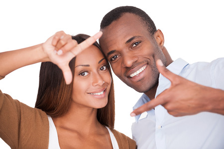 Focus on love. Handsome young African couple looking through a finger frame and smiling while standing isolated on white の写真素材