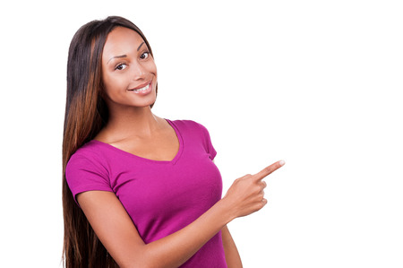 Pointing you advertising. Attractive young African woman pointing away and smiling while standing isolated on white の写真素材