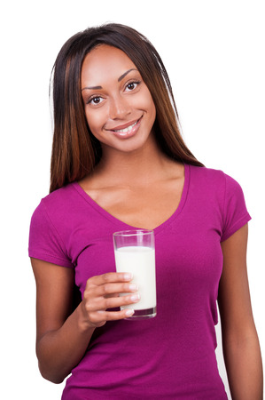 I love milk! Attractive young African woman holding a glass of milk and smiling at camera while standing isolated on white の写真素材