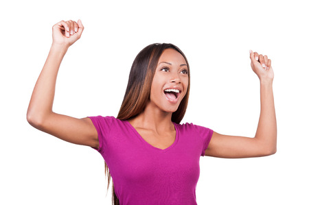 I am so happy! Beautiful young African woman keeping her arms raised and expressing positivity while standing isolated on white の写真素材