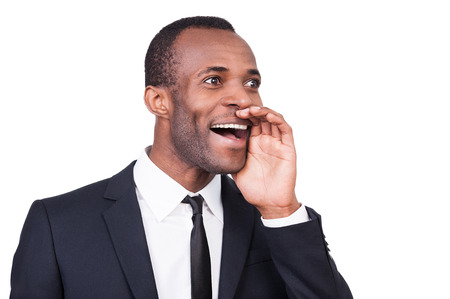 Announcing the good news. Cheerful young African man in formalwear holding hand near mouth and shouting while standing isolated on white background の写真素材