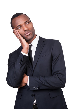 Business dreams. Thoughtful young African man in formalwear holding head in hand and looking away while standing isolated on white background の写真素材