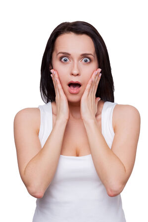 Shocking news. Surprised young woman holding head in hands and keeping mouth open while standing isolated on whiteの写真素材