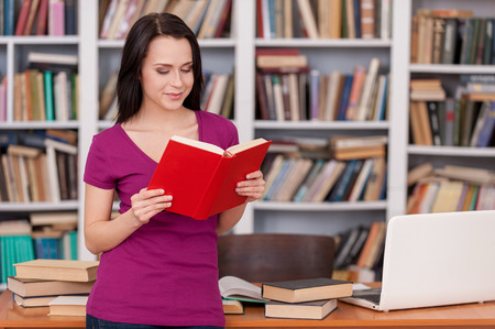 Woman in library. Cheerful young woman reading a book while leaning at the library deskの写真素材