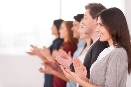People applauding. Side view of group of cheerful young people standing in a row and applauding to...
