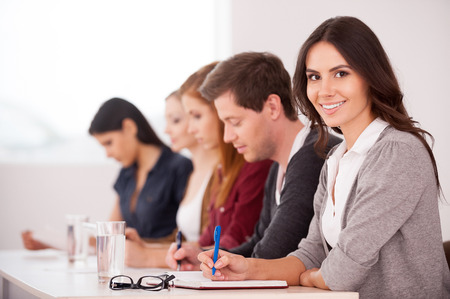 People at the seminar. Attractive young woman smiling at camera while sitting together with another people at the tableの写真素材