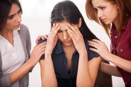 Feeling pain and depression. Depressed young woman sitting at the chair while two other women comforting herの写真素材