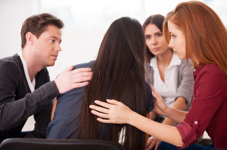 We understand you. Rear view of depressed young woman sitting at the chair while other people comforting herの写真素材