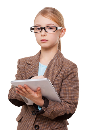 Little girl with digital tablet. Confident little girl in formalwear working on digital tablet and looking at camera while standing isolated on whiteの写真素材