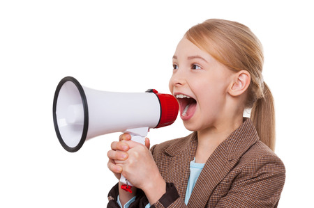 Announcing good news. Cheerful little girl in formalwear shouting at megaphone while standing isolated on whiteの写真素材