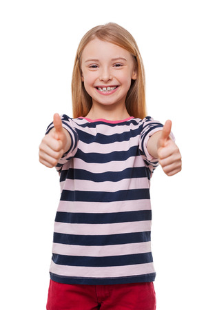 Happy little girl. Cheerful little girl showing her thumbs up while standing isolated on whiteの写真素材