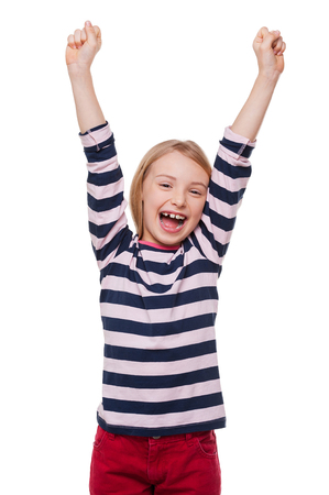 Happy little girl. Cheerful little girl keeping arms raised and smiling while standing isolated on whiteの写真素材