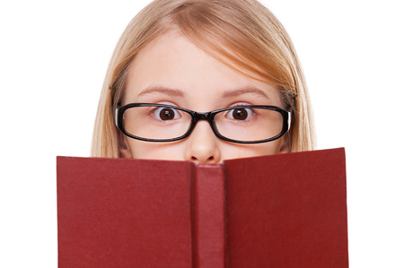 No way! Surprised little girl reading book and keeping mouth open while standing isolated on whiteの写真素材