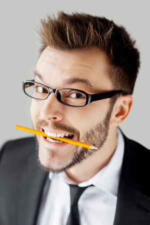 Creative and playful businessman. Playful young man in formalwear holding a pencil in mouth and looking at camera while standing against grey backgroundの写真素材