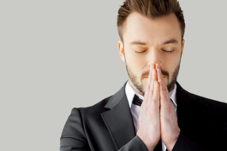 Businessman praying. Portrait of young man in formalwear holding hands clasped and keeping eyes...