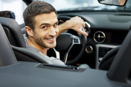 Happy cabriolet owner at the dealership. Handsome young men sitting at front seat of the car looking...