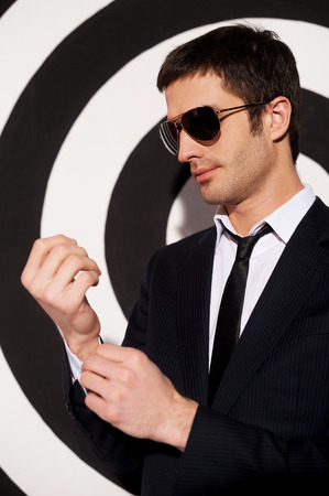 Confident in himself. Handsome young man in formalwear and sunglasses adjusting his shirt cuffs while standing against black and white background の写真素材