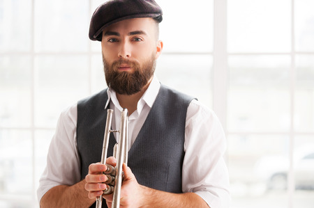 Ready for improvising. Handsome young bearded men standing with trumpet in his handsの写真素材