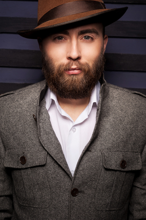 Thoughtful handsome. Portrait of handsome young man in hat looking at camera while standing against striped backgroundの写真素材