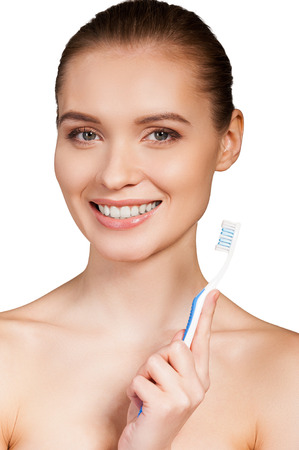 Keeping her teeth clean. Beautiful young woman holding toothbrush and smiling at camera while isolated on white backgroundの写真素材