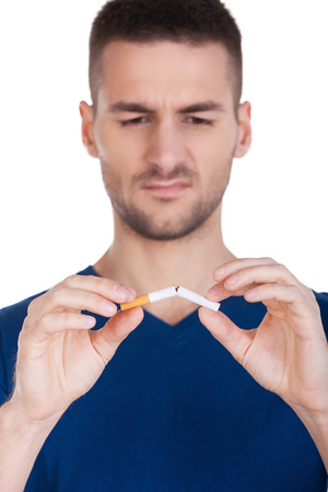 No more smoking. Serious young man holding scissors near the cigarette while standing isolated on white background の写真素材