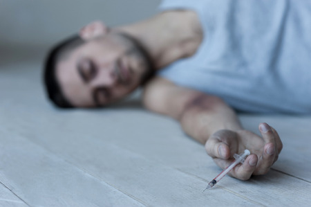 Young man lying on the floor and keeping eyes closed while holding syringe in his hand の写真素材