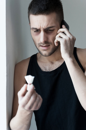  Frustrated young man holding a pack with heroin and talking on the mobile phoneの写真素材