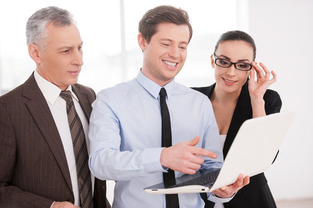Working on project together. Three confident business people discussing something while looking at the laptopの写真素材