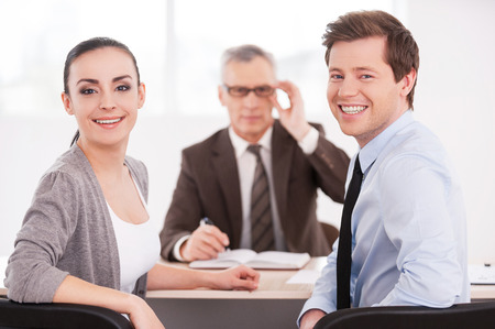 Successful business team. Confident business people looking at camera and smiling while sitting at the table together  の写真素材