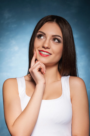 Waiting for inspiration. Beautiful young woman holding finger on chin and smiling の写真素材