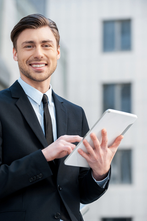 Successful businessman. Cheerful young men in formalwear holding digital tablet and looking at cameraの写真素材