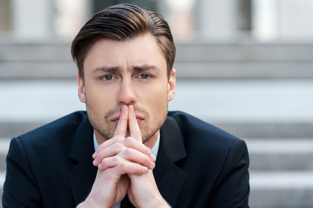 Thinking about solutions. Portrait of  young man in formalwear holding hands clasped and looking away while sitting outdoorsの写真素材