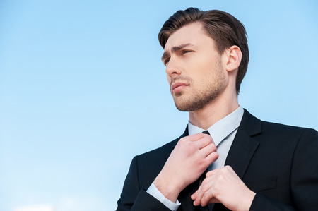 Cheerful businessman. Handsome young man in formalwear adjusting his necktie and looking awayの写真素材