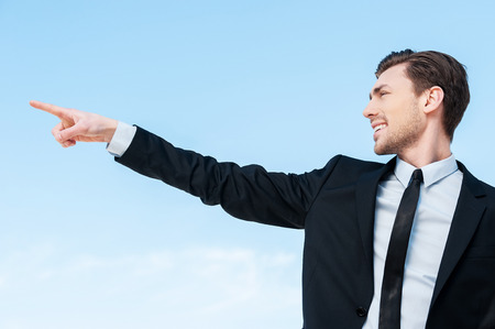There... Side view of a young businessman pointing at copy space against blue skyの写真素材