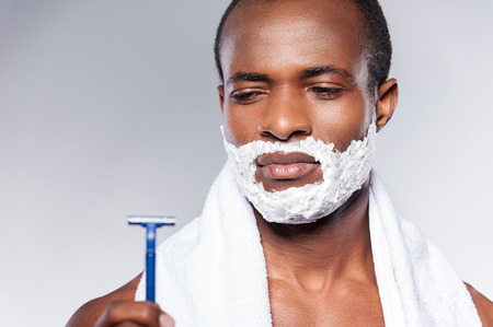 Really bad razor. Young shirtless African man looking at the razor and expressing negativity while standing against grey backgroundの写真素材