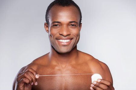 Handsome with dental floss. Portrait of young shirtless African man holding dental floss and smiling...