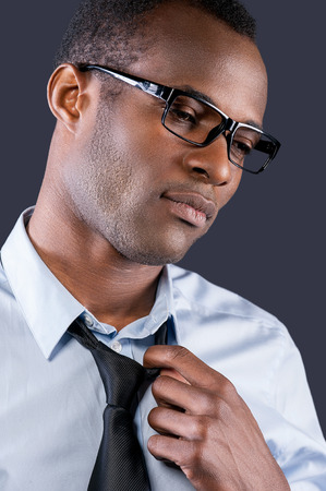 Taking his necktie off. Handsome young black man taking off his necktie while standing against grey backgroundの写真素材