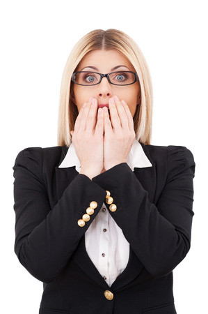 Shocked businesswoman. Shocked mature businesswoman covering mouth with hands and looking at camera while standing isolated on whiteの写真素材