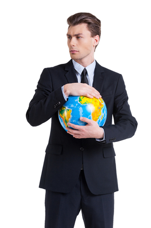 World in his hands. Confident young man in formalwear holding globe and looking away while standing isolated on whiteの写真素材
