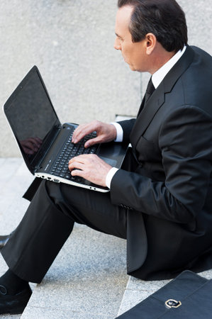 Concentrated on work. Confident senior man in formalwear working on laptop while sitting outdoorsの写真素材