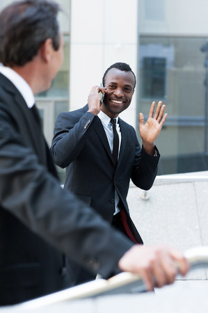 Hello! Cheerful young African man in formalwear moving up by stairs and waving to his colleague の写真素材